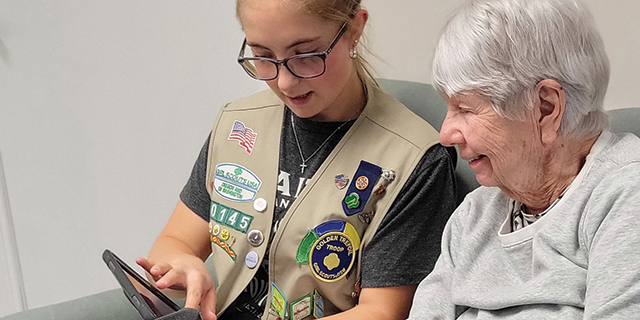Maylie Eby, left, demonstates how to use the tablet where her project for her Girl Scout Gold Award is stored at Grande Ronde Retirement in La Grande. Eby worked with Island City Elementary School to film fourth and fifth graders reading, which older adults at the retirement home can watch on the tablets. (Girl Scout Troop No. 50145/Contributed Photo)